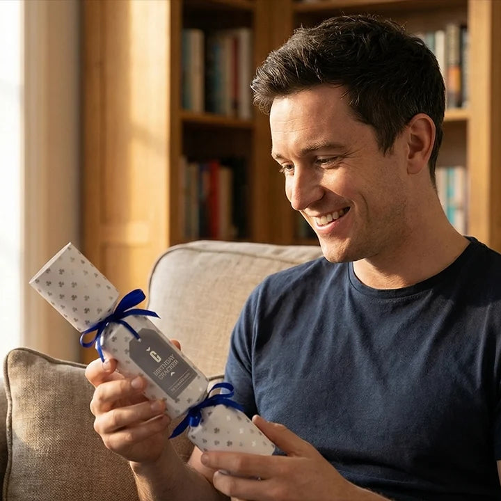 Lächelnder Mann öffnet ein eingepacktes Geburtstagsgeschenk auf dem Sofa – Geschenkideen zum Geburtstag von Hope22