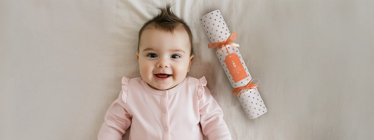 Baby im rosa Strampler liegt neben einer verpackten Geschenkrolle – Geschenke zur Geburt von Hope22