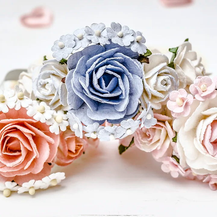 Drei Hope22 Blumenarmbänder mit Rosen in Rosé, Blau und Creme auf hellem Holz mit Herzdeko – Armbänder für JGA und Hochzeit