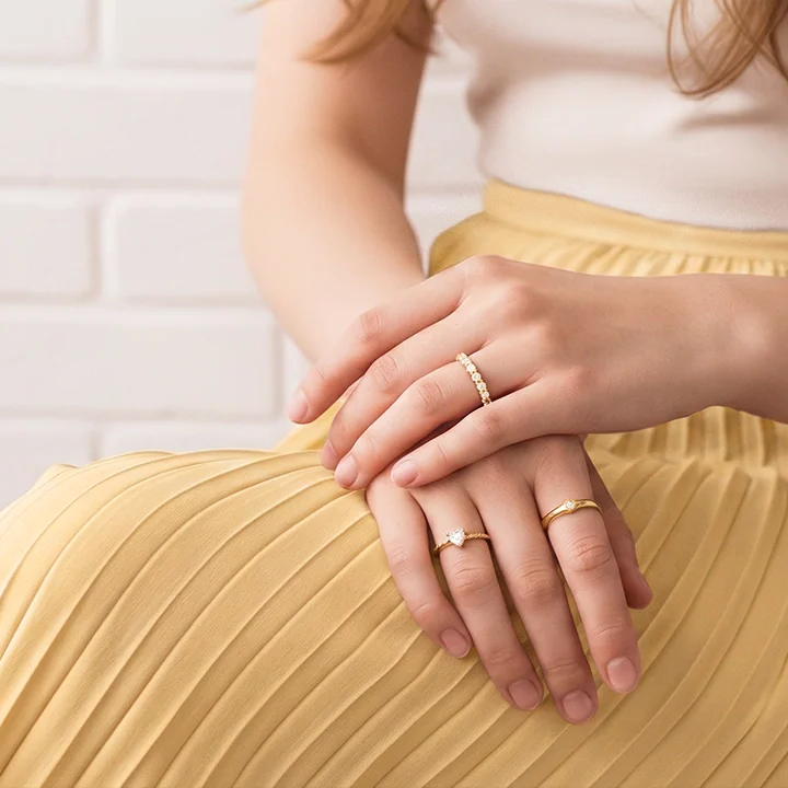 Frauenhände mit zarten goldenen Ringen auf gelbem Plisseerock – Ringe für Damen von Hope22