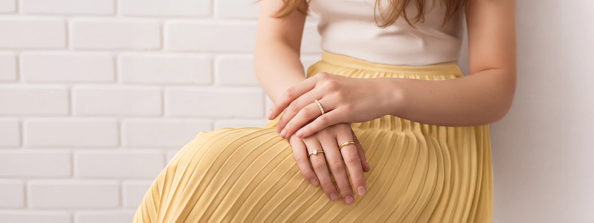 Frauenhände mit zarten goldenen Ringen auf gelbem Plisseerock – Ringe für Damen von Hope22