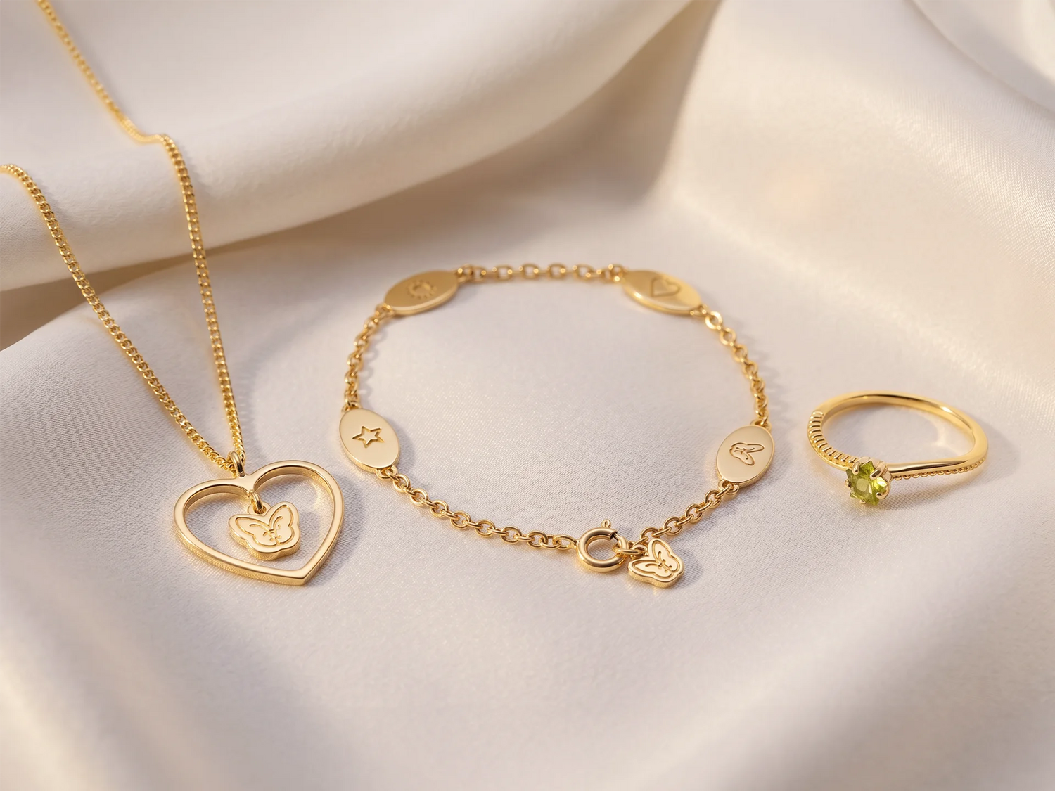 Hope22 Goldschmuck-Set auf cremefarbener Seide – Herzkette mit Schmetterling, Gliederarmband und Ring mit grünem Stein